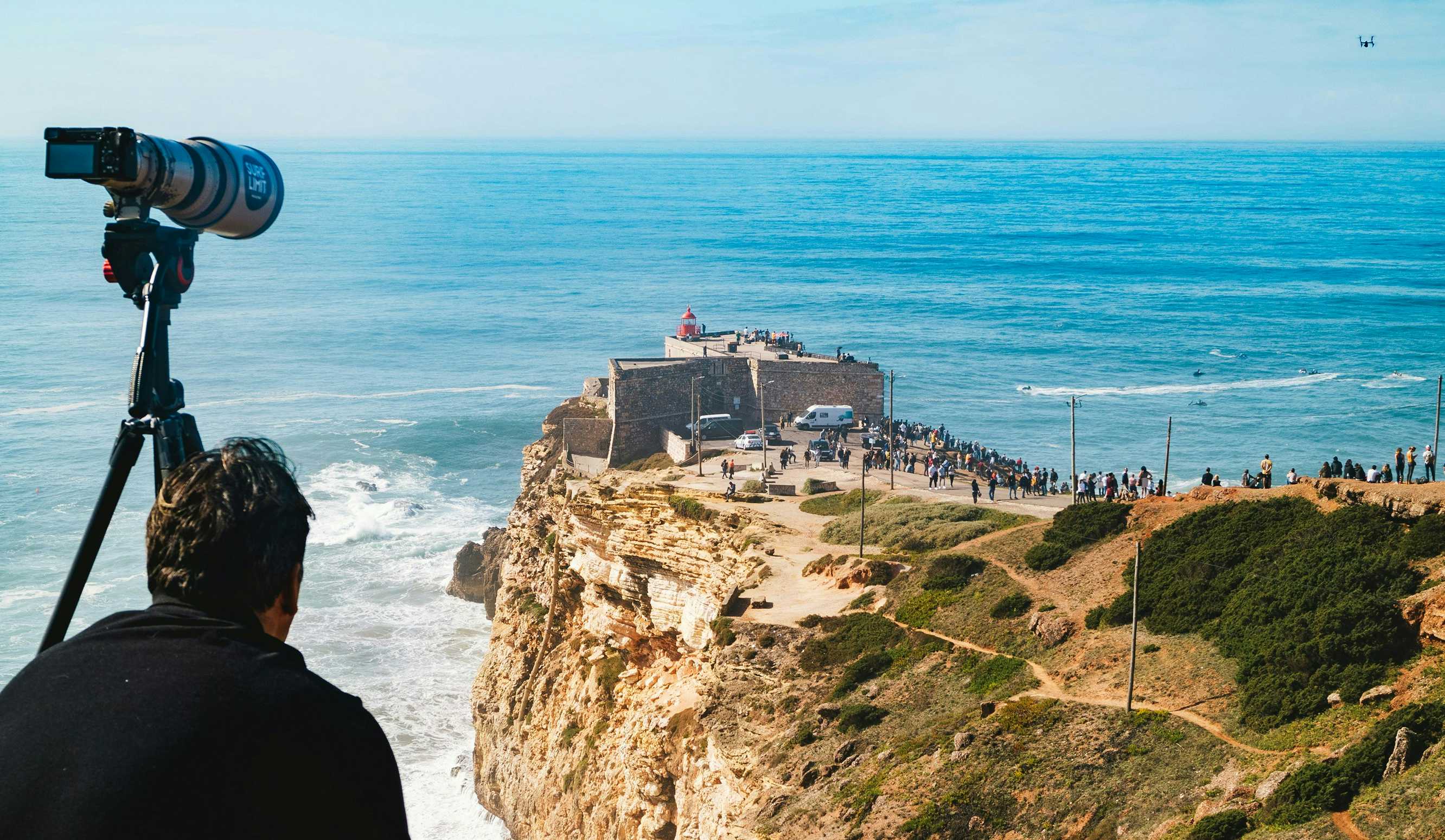 Fotografo de surf sentado olhando para praia de nazaré em portugal.